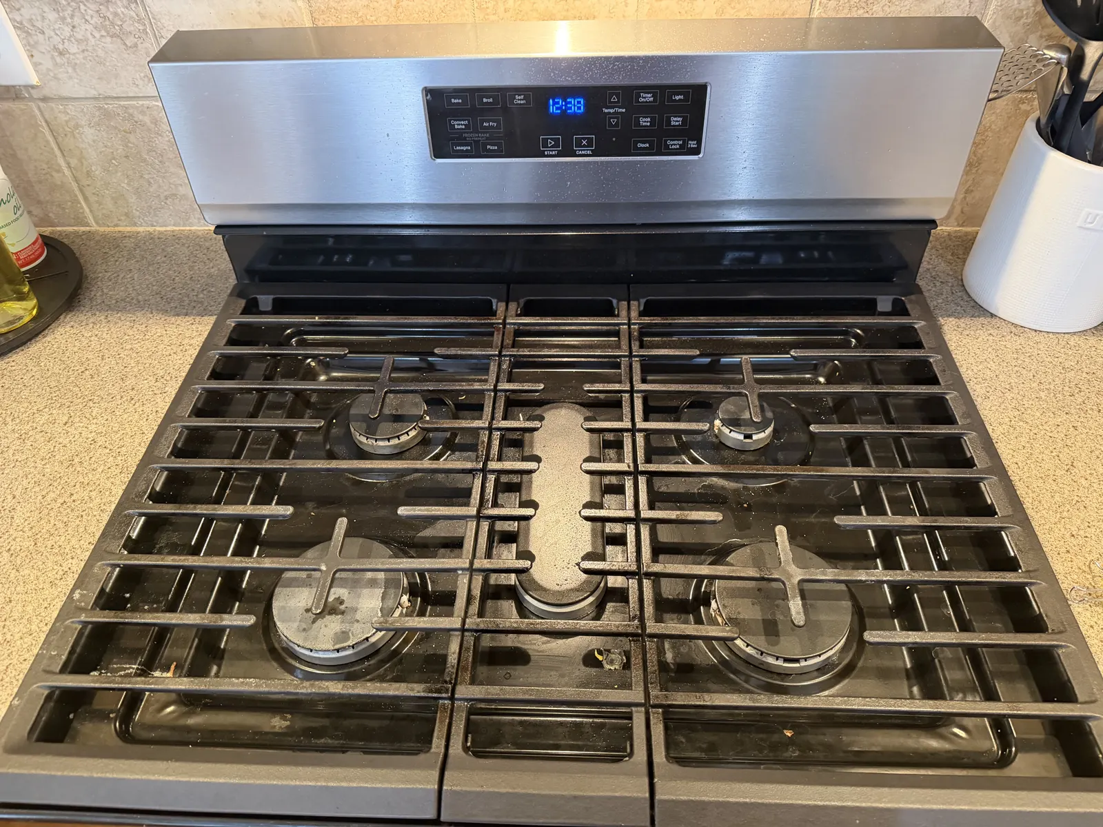 A gas stovetop before cleaning, with grease and burnt-on spills around the burners